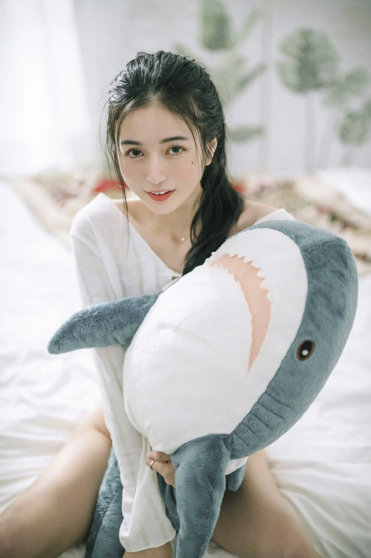 辰辰身着白色深V领上衣双手环抱灰白鲨鱼玩偶正面照